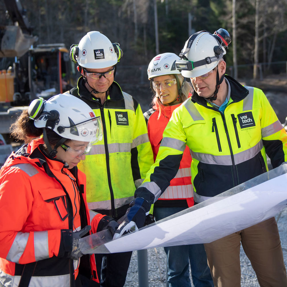 Flera personer i varselkläder samtalar kring en ritning.