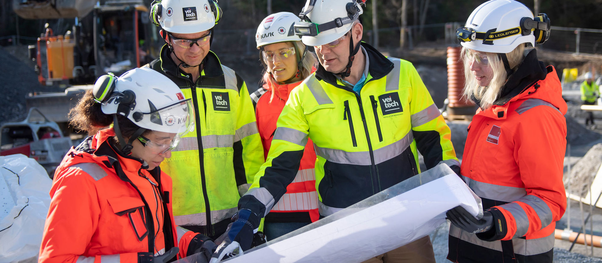 Flera personer i varselkläder samtalar kring en ritning.